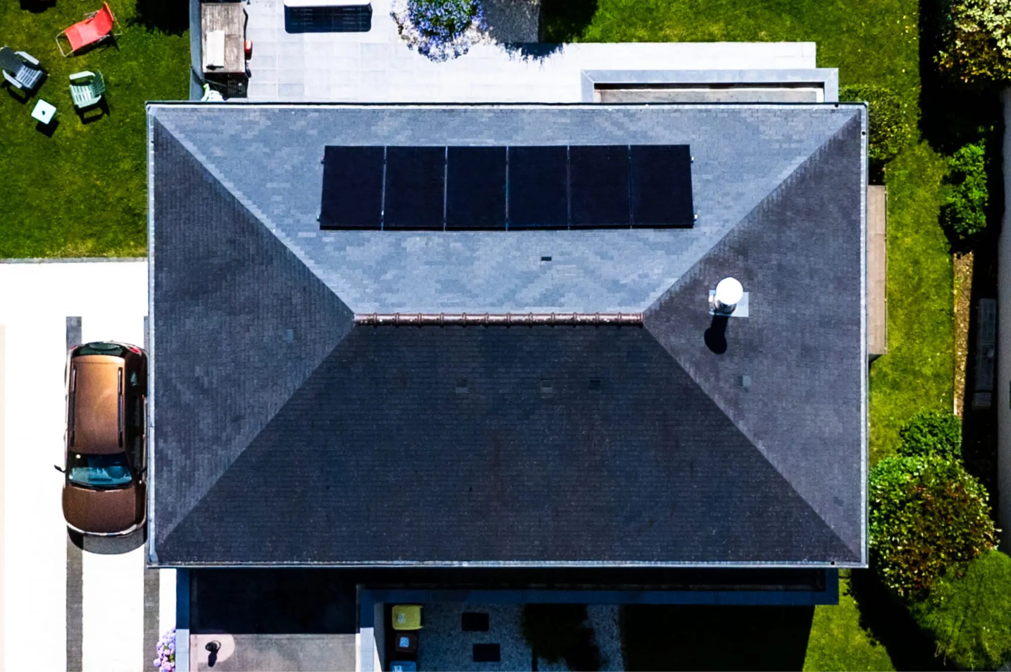 Vue aérienne par drone d’une toiture en ardoise équipée de panneaux solaires Sunology, montrant l’intégration harmonieuse des modules solaires sur le toit traditionnel sous un ciel bleu clair.