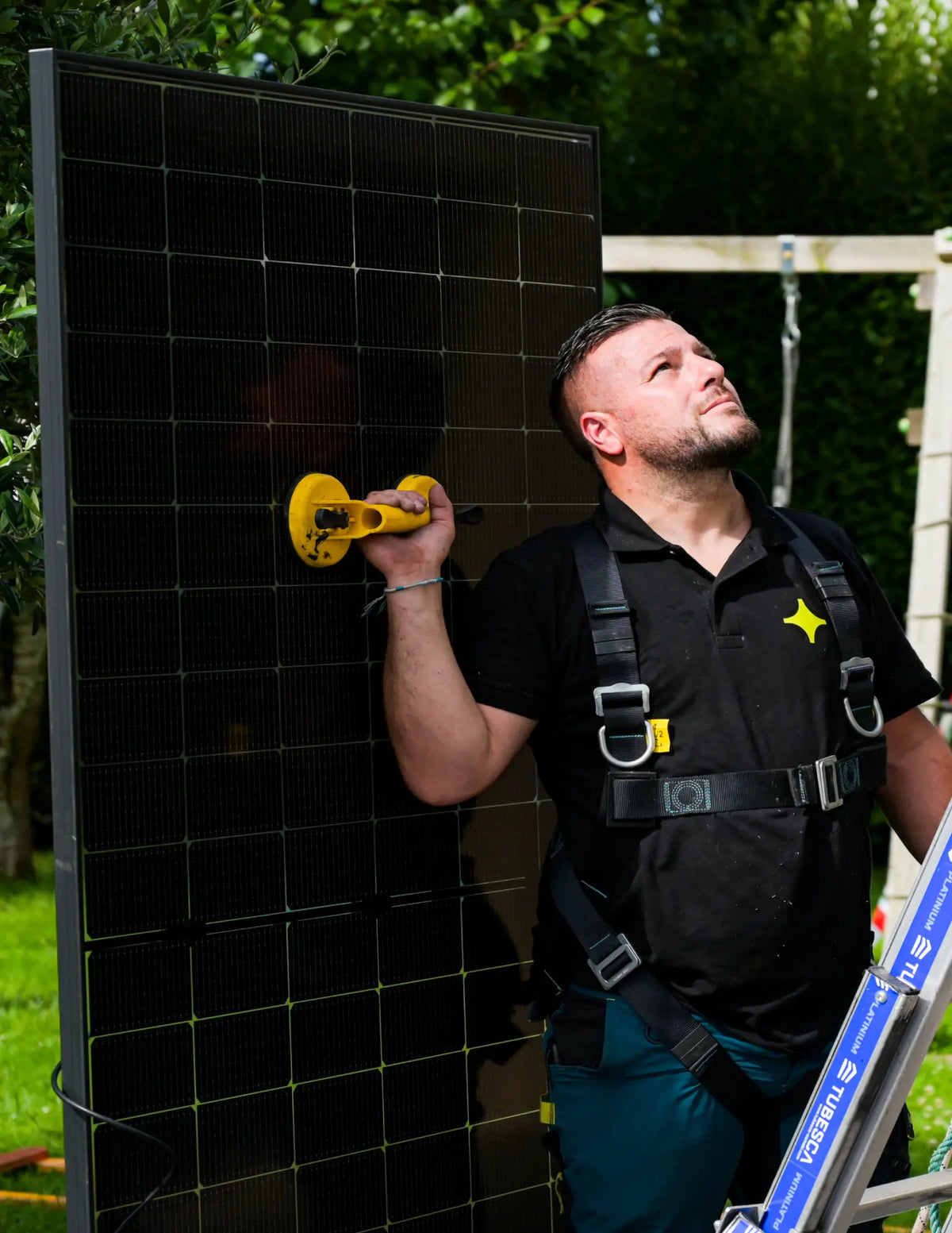 Artisan Sunology HOME portant un panneau solaire photovoltaïque, prêt à être posé sur une toiture en ardoise. L’image montre le professionnel en tenue de travail, avec un ciel clair en arrière-plan, illustrant la pose soignée et experte des modules solaires.