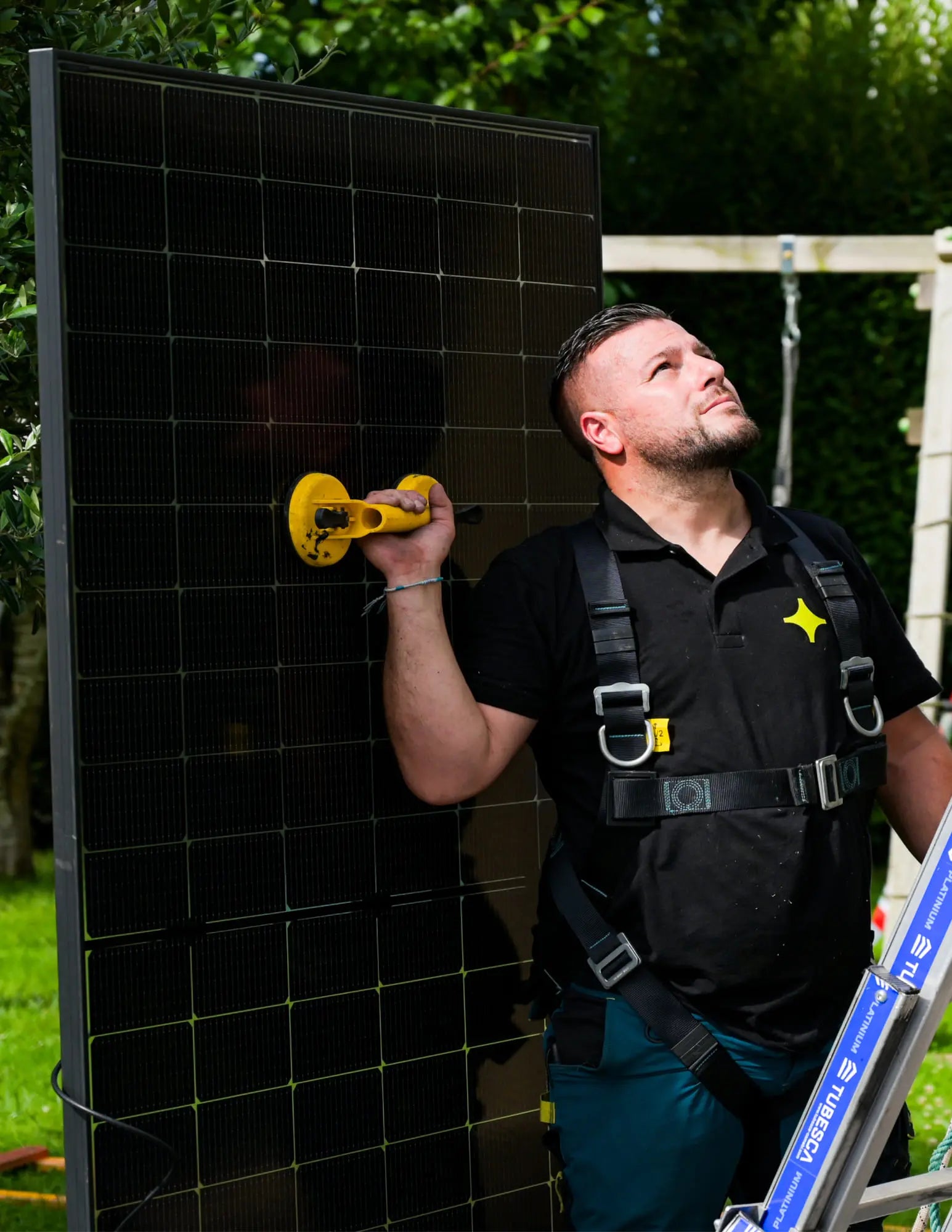 Artisan Sunology HOME portant un panneau solaire photovoltaïque, prêt à être posé sur une toiture en ardoise. L’image montre le professionnel en tenue de travail, avec un ciel clair en arrière-plan, illustrant la pose soignée et experte des modules solaires.