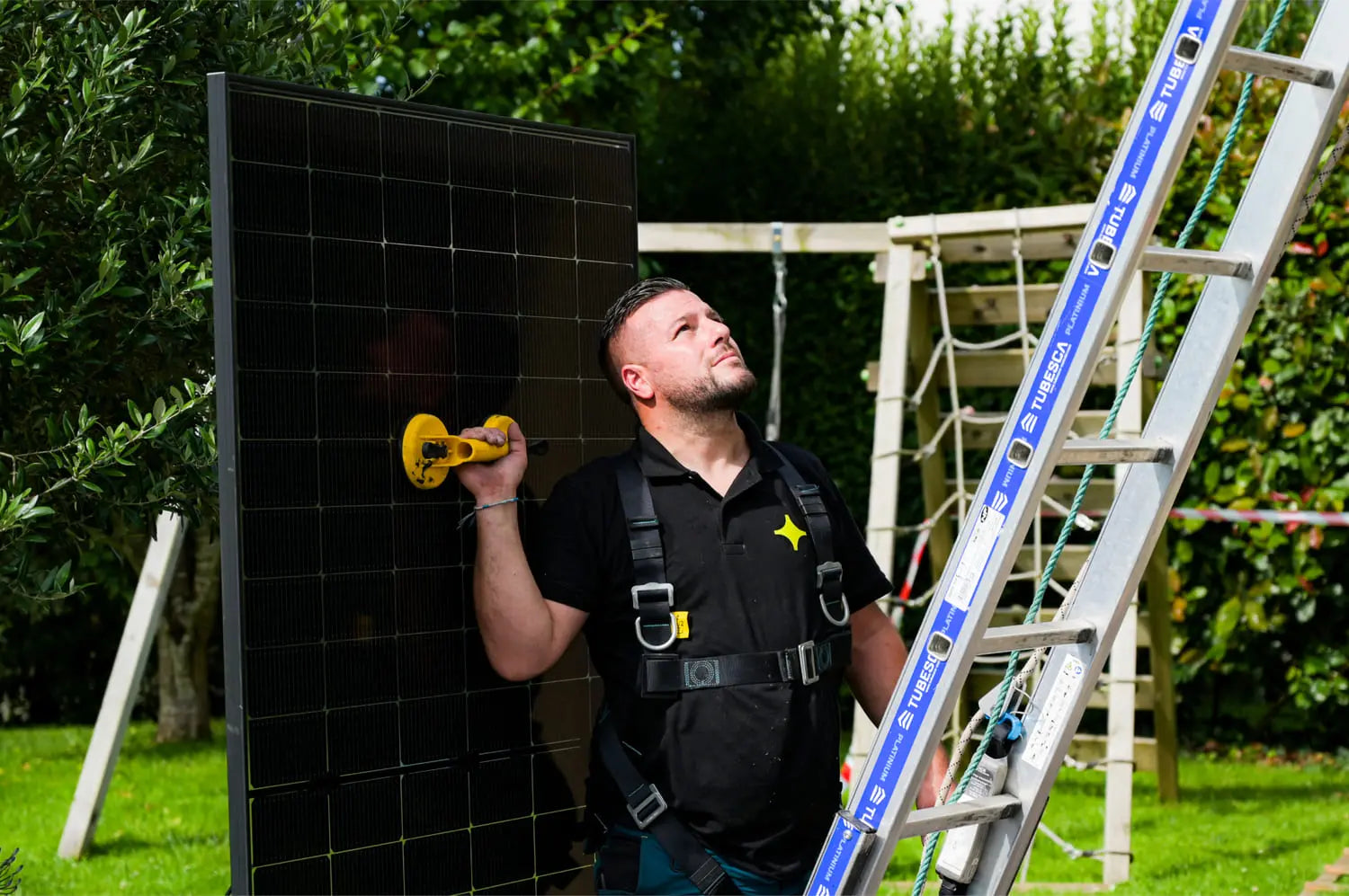 Artisan Sunology HOME portant un panneau solaire photovoltaïque, prêt à être posé sur une toiture en ardoise. L’image montre le professionnel en tenue de travail, avec un ciel clair en arrière-plan, illustrant la pose soignée et experte des modules solaires.
