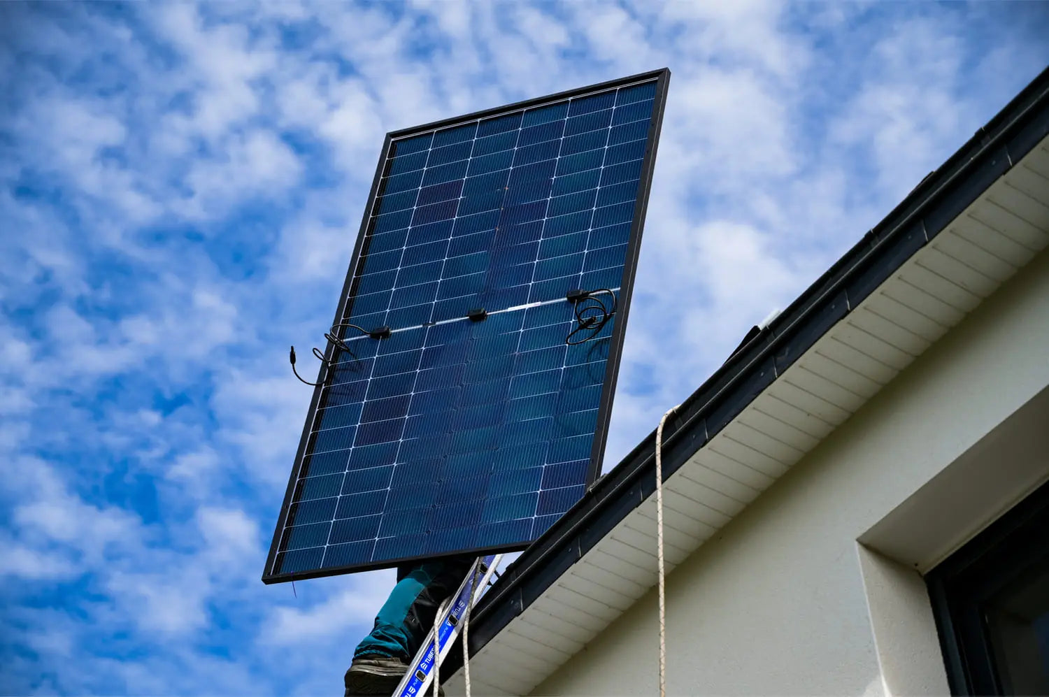 Artisan Sunology HOME portant un panneau solaire photovoltaïque, prêt à être posé sur une toiture en ardoise. L’image montre le professionnel en tenue de travail, avec un ciel clair en arrière-plan, illustrant la pose soignée et experte des modules solaires.