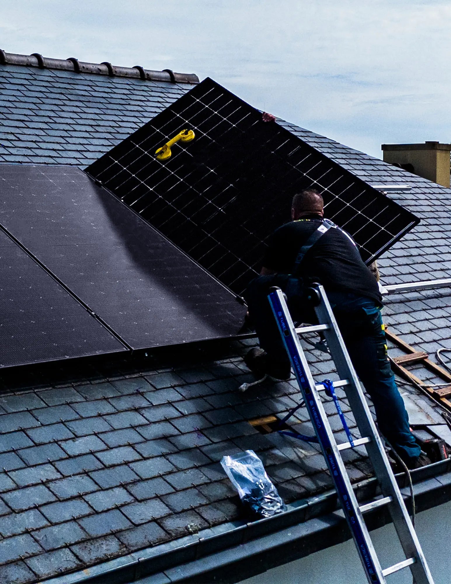Installateurs Sunology HOME en pleine installation de panneaux solaires sur une toiture en ardoise. On voit plusieurs techniciens équipés de harnais de sécurité posant avec précision les modules solaires sur la toiture traditionnelle, sous un ciel dégagé. L’image illustre un travail soigné et professionnel, alliant modernité énergétique et respect du patrimoine architectural.
