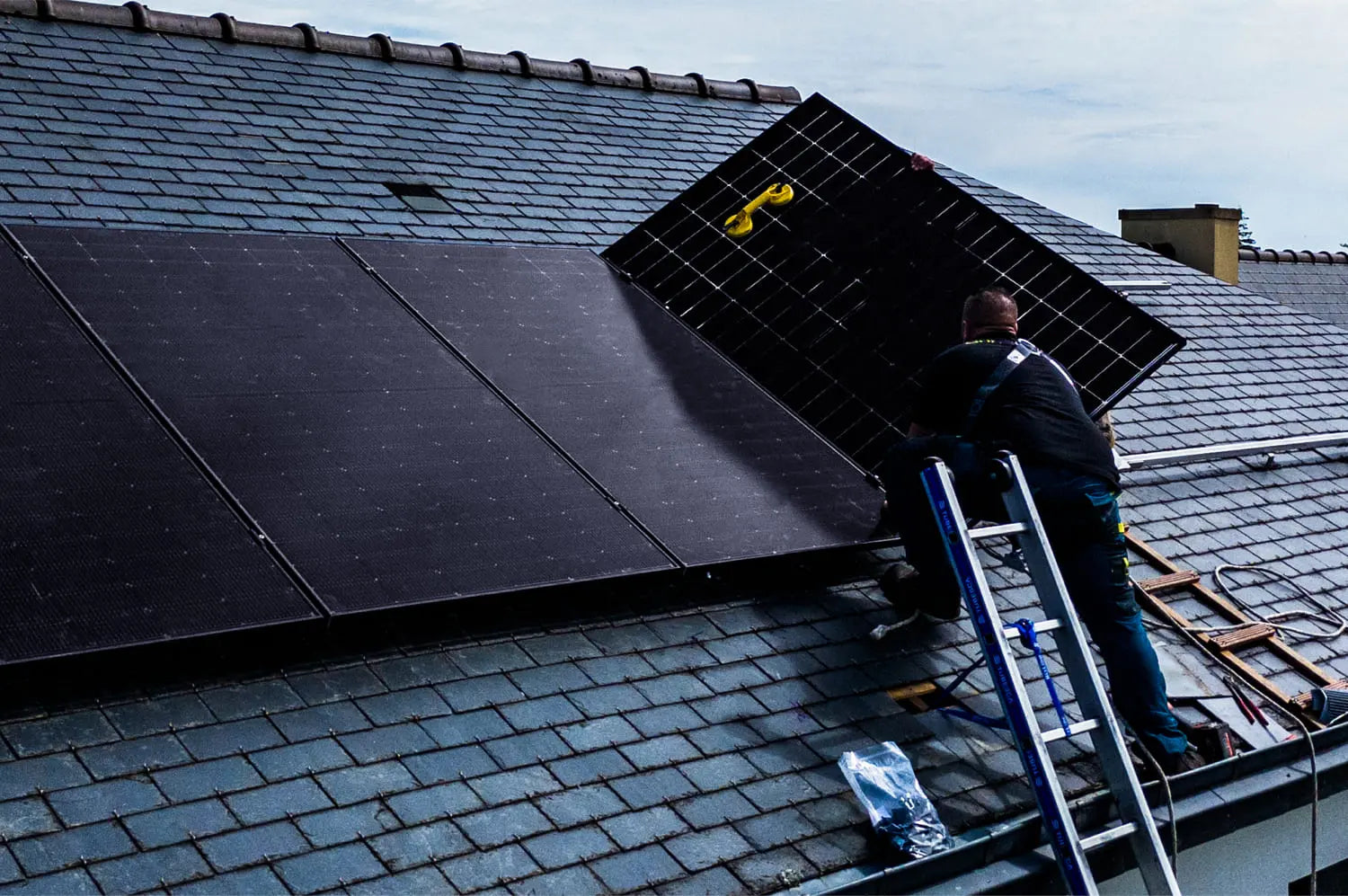 Installateurs Sunology HOME en pleine installation de panneaux solaires sur une toiture en ardoise. On voit plusieurs techniciens équipés de harnais de sécurité posant avec précision les modules solaires sur la toiture traditionnelle, sous un ciel dégagé. L’image illustre un travail soigné et professionnel, alliant modernité énergétique et respect du patrimoine architectural.