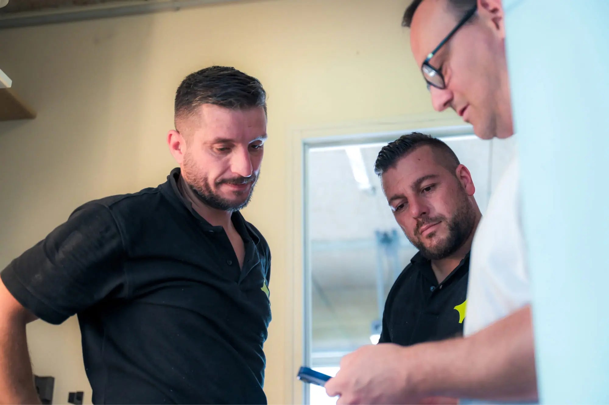 Artisans Sunology expliquant le fonctionnement de la toiture solaire et présentant l’application de suivi à un client. Ils montrent l’écran d’une tablette, illustrant les données en temps réel, dans un cadre convivial et professionnel.