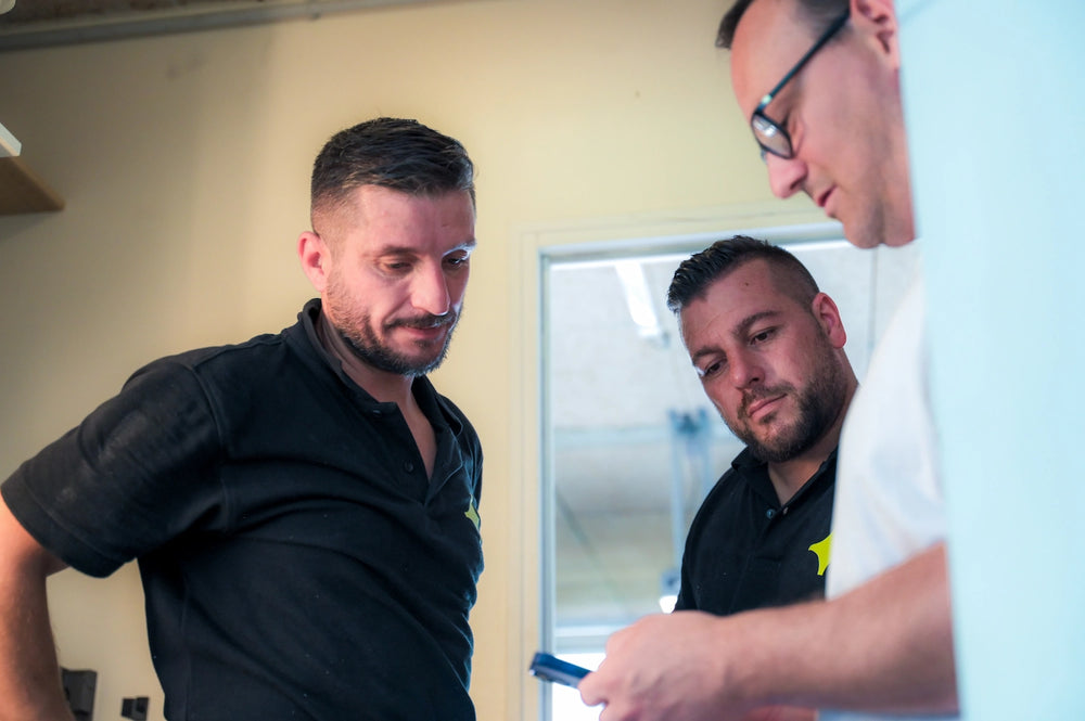 Artisans expliquant au client l’utilisation de l’application de suivi de production, démonstration app chantier, gestion projet travaux, communication client-artisans, suivi en temps réel, outil digital chantier, collaboration efficace, transparence travaux, gestion opérationnelle, optimisation production, interface intuitive, suivi de projet bâtiment, application métier artisans, relation client professionnelle.
